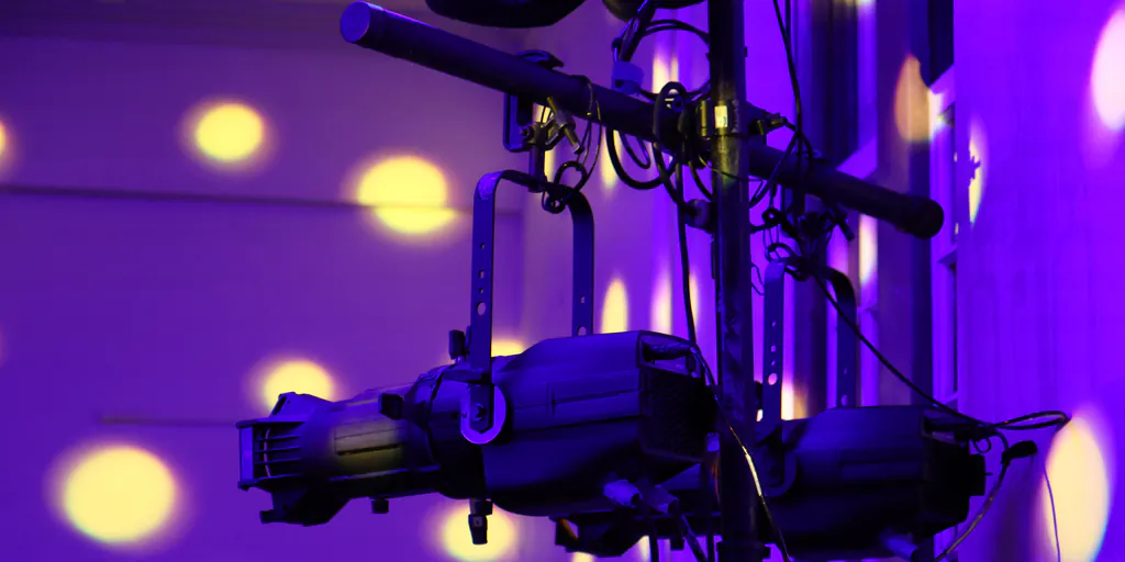 Two ellipsoidal spotlights hung on a crossbar, running, throwing a warm break-up pattern across a hall wall.
